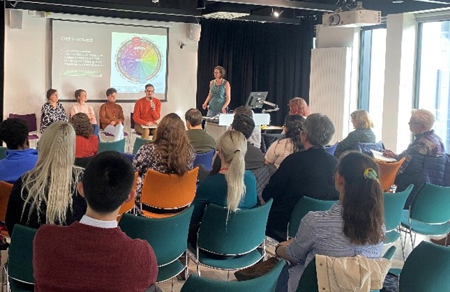 Photo from the Diversity in Data Science group launch. We can see four panellists in the background discussing their work on intersectionality and inclusivity in data science, while Sal (the chair) poses questions. In the foreground we can see a packed audience of interested researchers and professional services staff.